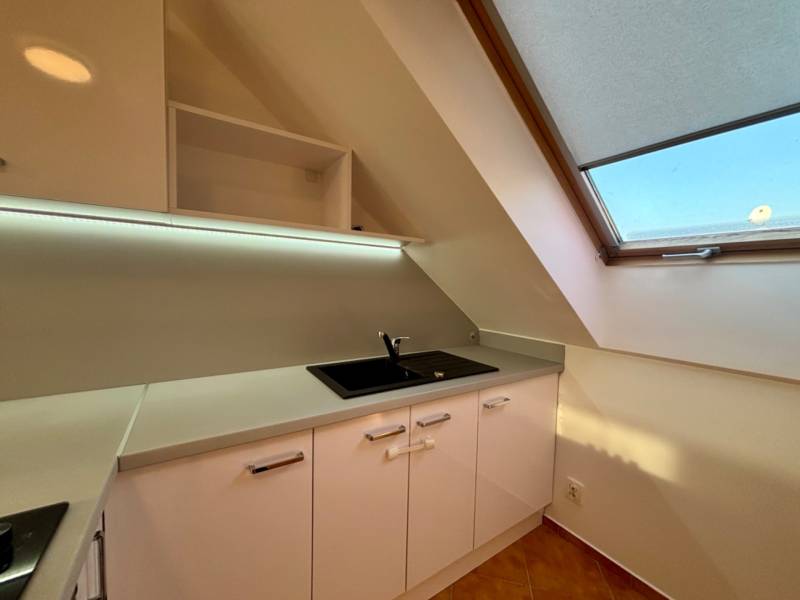 Eine Küchenzeile in einer 2-Zimmer-Wohnung mit weißen Schränken und einem großen Dachfenster.