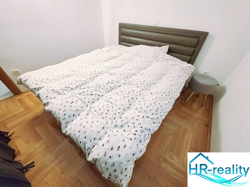 Ferienwohnung mit Bett, Holzboden-Dekor und kleinem Nachttisch.