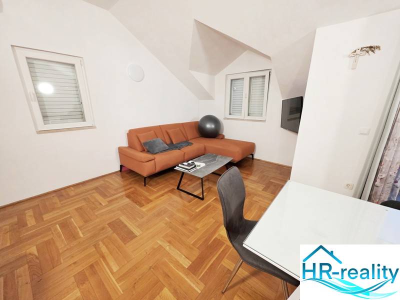 Ferienwohnung mit orangefarbenem Sofa und Boden in Holzoptik.