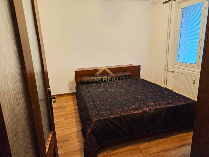 Schlafzimmer in einer 3-Zimmer-Wohnung mit Holzboden und dunkler Bettüberdecke.