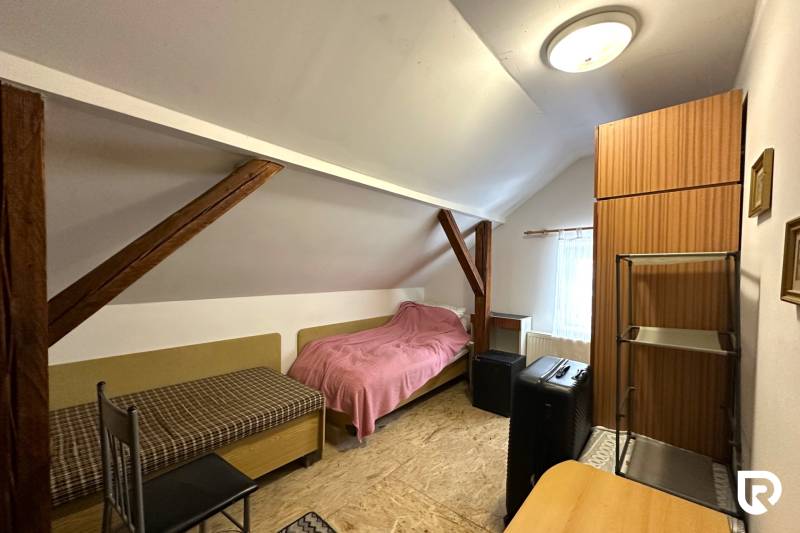 Ein Dachzimmer in einem Einfamilienhaus mit einfacher Möblierung und Dachbalken.