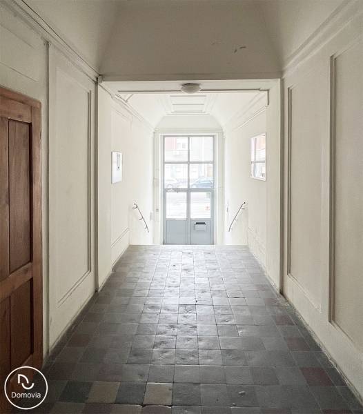 Ein Flur mit Fliesen und weißen Wänden führt zu einer verglasten Tür zur Vajnorská-Straße.