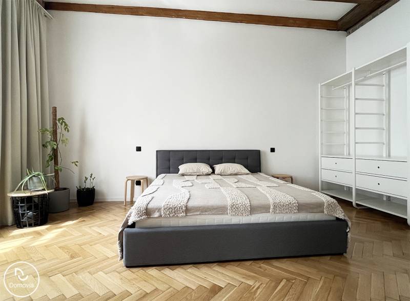 Ein stilvolles Schlafzimmer mit einem Bett in einer 2-Zimmer-Wohnung, Pflanzen und Stauraum in der Vajnorská-Straße.