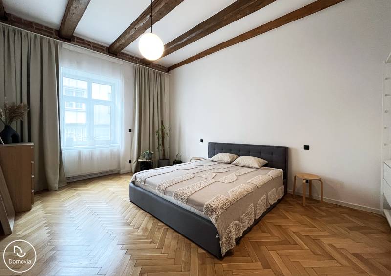 Helles Schlafzimmer mit Holzbalken, bequemem Bett und Parkettboden in der Vajnorská-Straße.