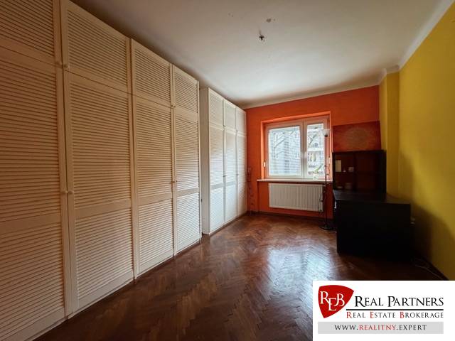 Ein Zimmer mit einer orangefarbenen Wand, einem großen Schrank und einem Boden mit Holzdekor in einer 3-Zimmer-Wohnung.