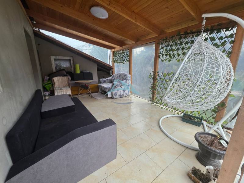 Terrasse in einem Einfamilienhaus in Hont mit Schaukel, Sofa und Korbsessel.