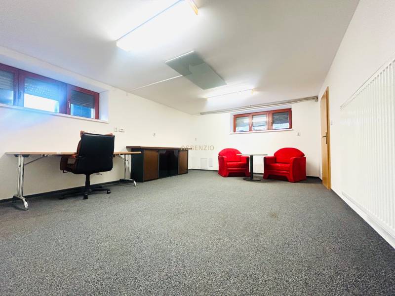 Das Büro im Einfamilienhaus hat einen Teppich, einen Schreibtisch und rote Sessel.