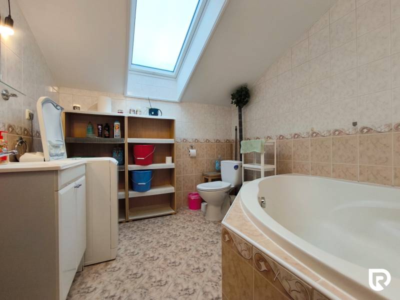Badezimmer in einem Einfamilienhaus mit Badewanne, Waschmaschine, Regal und Dachfenster.