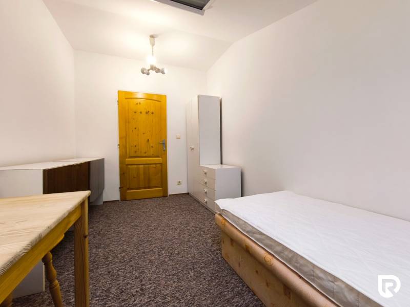 Ein Zimmer in einem Einfamilienhaus mit einem Bett, einem Schrank und einem Tisch, ergänzt durch weiße Beleuchtung und Teppichboden.