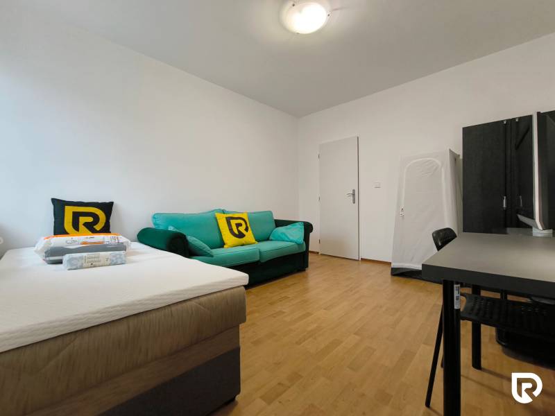 Ein Zimmer in einem Einfamilienhaus mit einem Bett, einem Sofa und einem Schreibtisch, Boden mit Holzdekor.