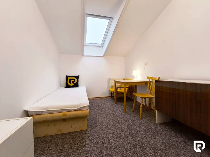 Einfaches Zimmer mit Einzelbett, Tisch und Stühlen in einem Einfamilienhaus.