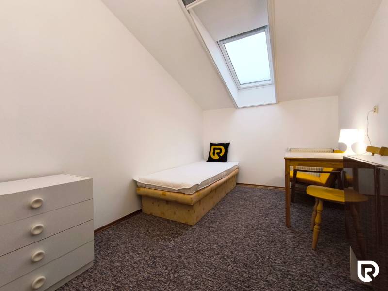 Einfaches Zimmer mit einem Bett, einem Tisch und einer Kommode in einem Einfamilienhaus.