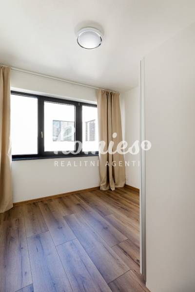 Ein Zimmer in einer 3-Zimmer-Wohnung mit einem Boden in Holzoptik und einem Fenster mit Vorhang.