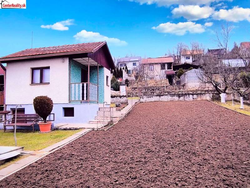 Hütte in Partizánske mit Garten und frisch gepflügtem Boden, mit einer Bank und Sträuchern.