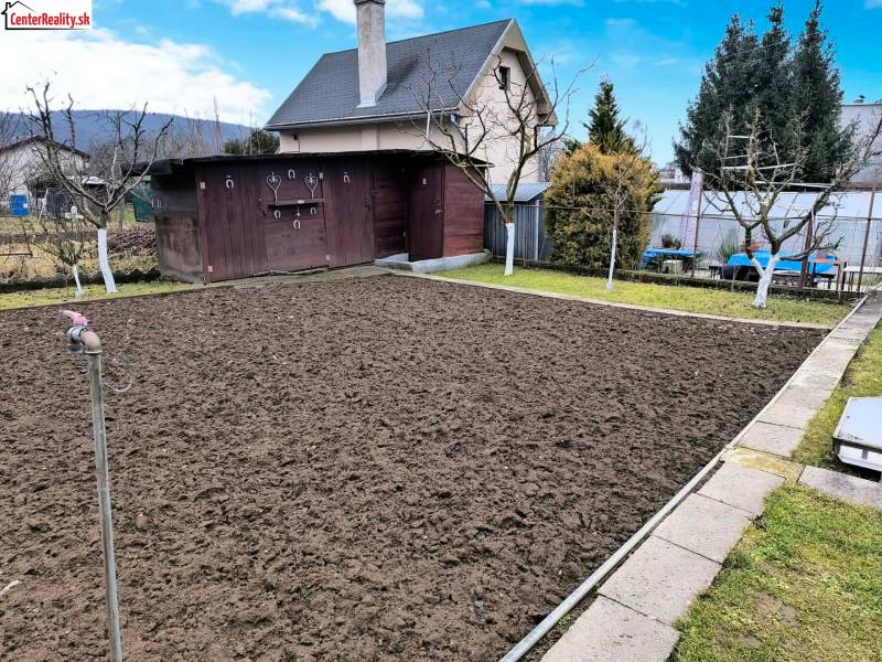 Garten mit Hütte in Partizánske, vorbereitetes Beet, umliegendes Grün und Holzhaus.