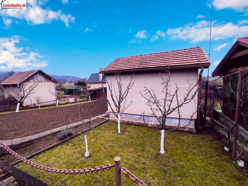 Ein Garten mit einer Hütte in Partizánske, Obstbäume und bewirtschaftetes Land, klarer Himmel.