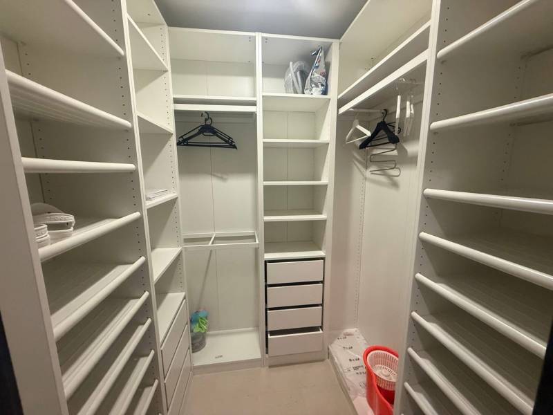 Ein Kleiderschrank in einer 3-Zimmer-Wohnung mit weißen Regalen und Wandhaken.