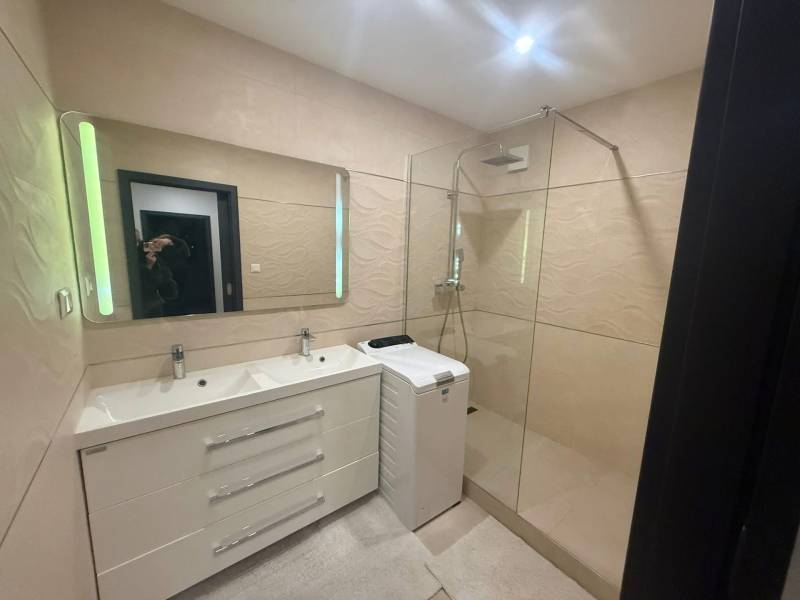 Badezimmer mit Doppelwaschbecken, Duschkabine und Waschmaschine in einer 3-Zimmer-Wohnung.