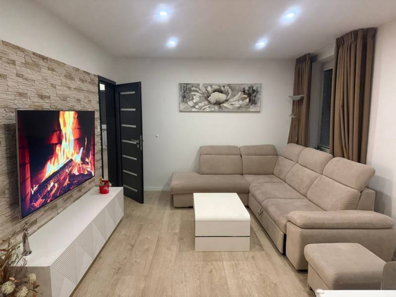 Wohnzimmer einer 3-Zimmer-Wohnung mit beigem Sofa, Fernseher und Boden in Holzoptik.