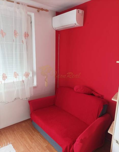 Rotes Sofa, Wandklimaanlage und Vorhang in einem Einzimmerapartment mit Holzboden.