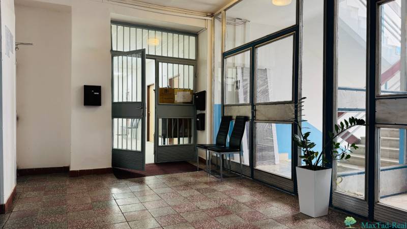 Eingang zum Büro mit Glastüren, Pflanze und Sitzgelegenheit.