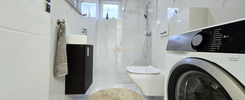 Badezimmer in einem Einfamilienhaus mit Waschmaschine und Duschkabine, elegante Fliesen.