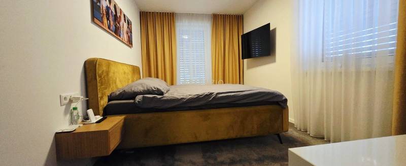 Schlafzimmer in einem Einfamilienhaus mit Bett, Nachttisch, Fernseher und Vorhängen.