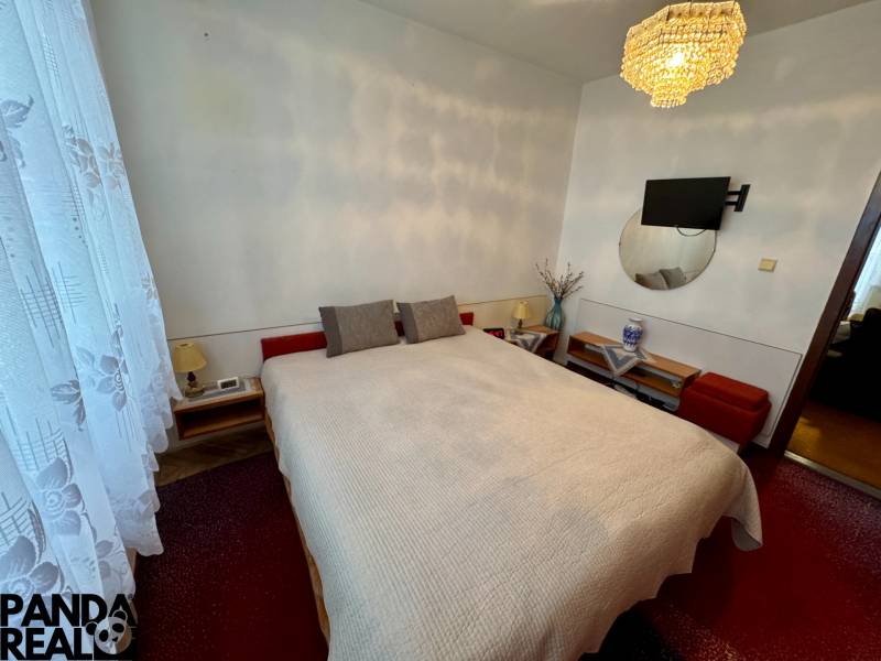 Schlafzimmer in einer 3-Zimmer-Wohnung mit Bett, Kronleuchter und Fernseher an der Wand.