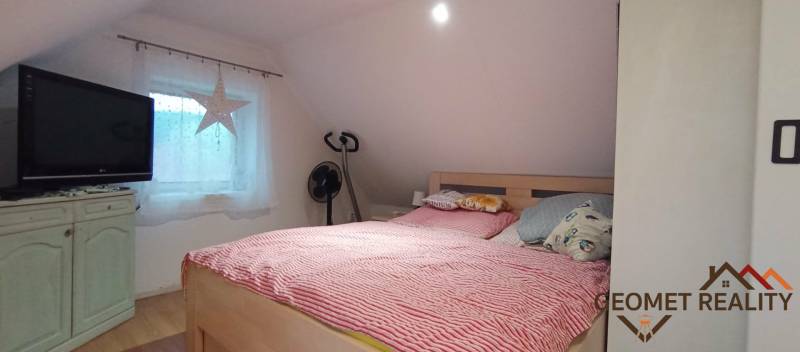 Ein Schlafzimmer im Dachgeschoss eines Einfamilienhauses mit Bett, Fernseher und einem Boden in Holzoptik.