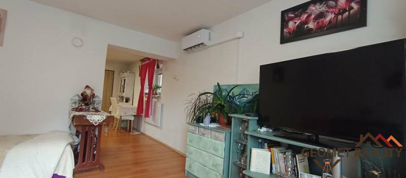 Wohnzimmer mit Holzboden, Fernseher, Klimaanlage und dekorativen Elementen.