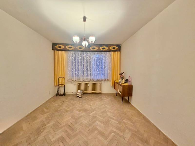 Ein Zimmer in einer 3-Zimmer-Wohnung mit einem Boden in Holzoptik, Vorhängen und einer Kommode.