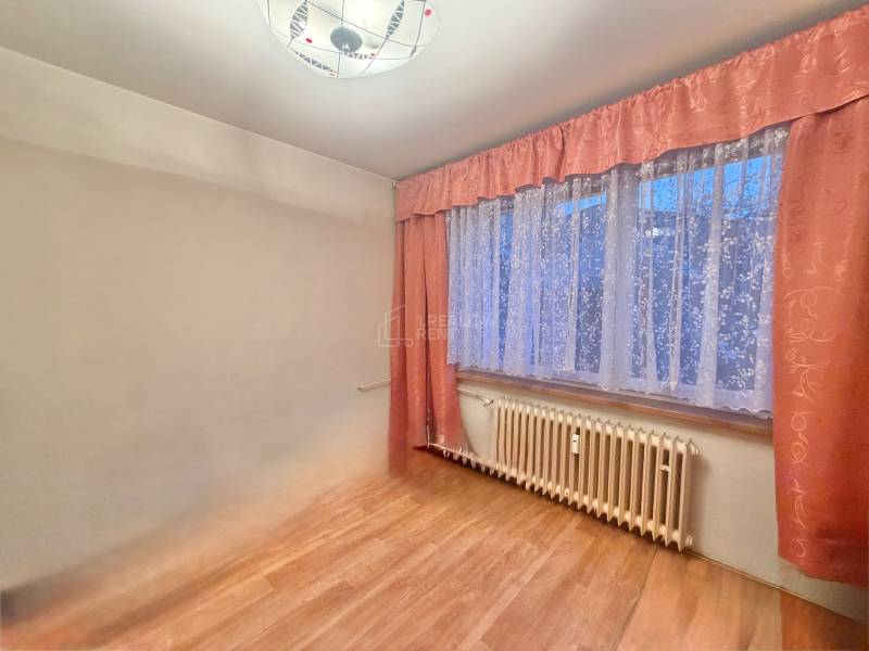 Ein Zimmer in einer 3-Zimmer-Wohnung mit einem Boden in Holzoptik und Vorhängen.