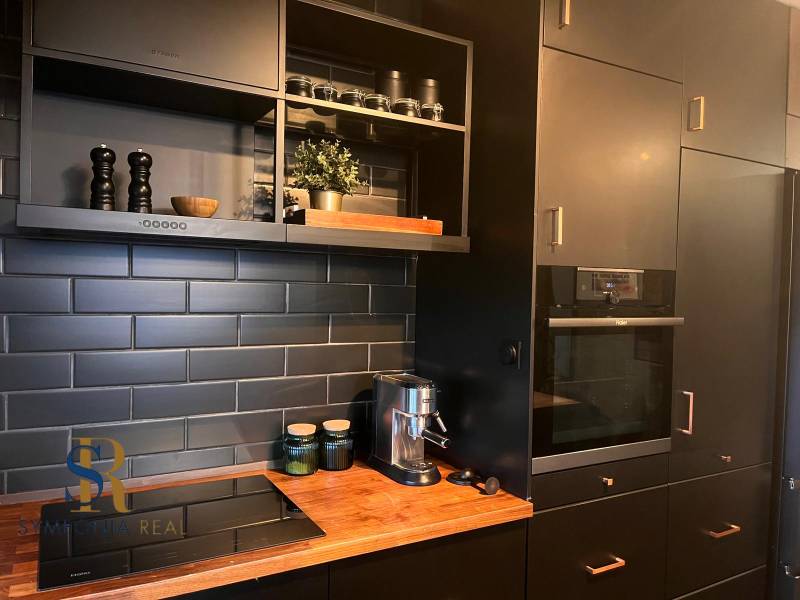 Küche mit schwarzen Schränken in einer 2-Zimmer-Wohnung und einem Boden mit Holzdekor.