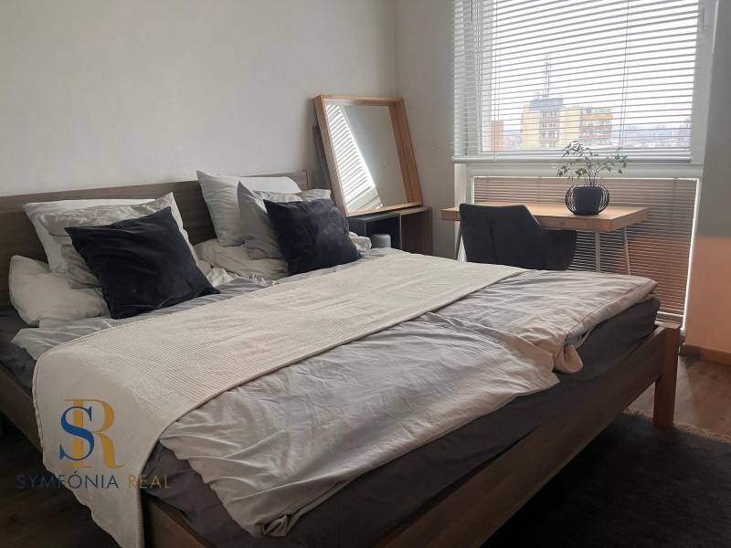 Schlafzimmer in einer 2-Zimmer-Wohnung mit Bett, Schreibtisch und Boden in Holzoptik.