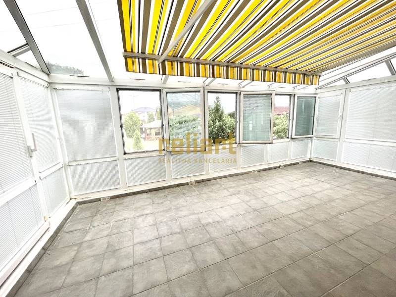 Wintergarten in einem Einfamilienhaus mit großen Fenstern und gelb gestreiften Rollläden.