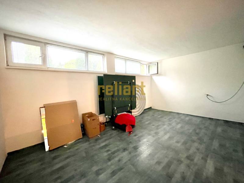 Ein Zimmer in einem Einfamilienhaus mit einem Boden in Holzoptik, Fenstern und Pappkartons.