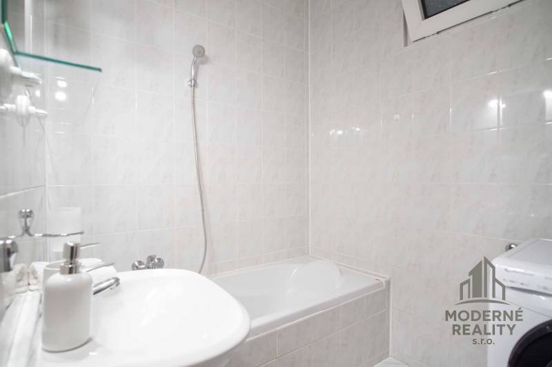 Badezimmer mit Badewanne und Waschmaschine in einer 4-Zimmer-Wohnung. Wände mit hellen Fliesen bedeckt.