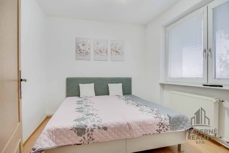 Schlafzimmer mit hellem Bett, Boden mit Holzdekor und dekorativen Bildern in einer 4-Zimmer-Wohnung.