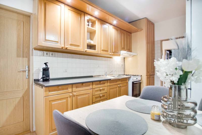 Küche in einer 4-Zimmer-Wohnung mit Holzschränken, Blumen und Esstisch.