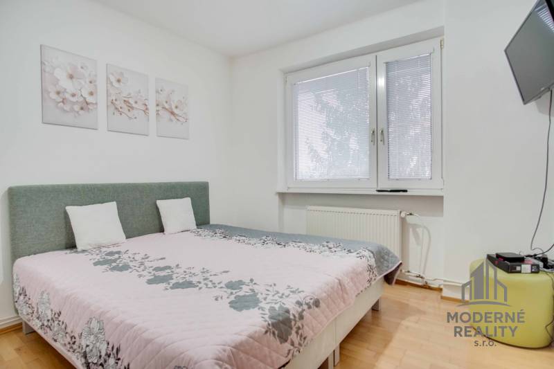 Schlafzimmer in einer 4-Zimmer-Wohnung mit Blumendekorationen und einem Fernseher an der Wand.