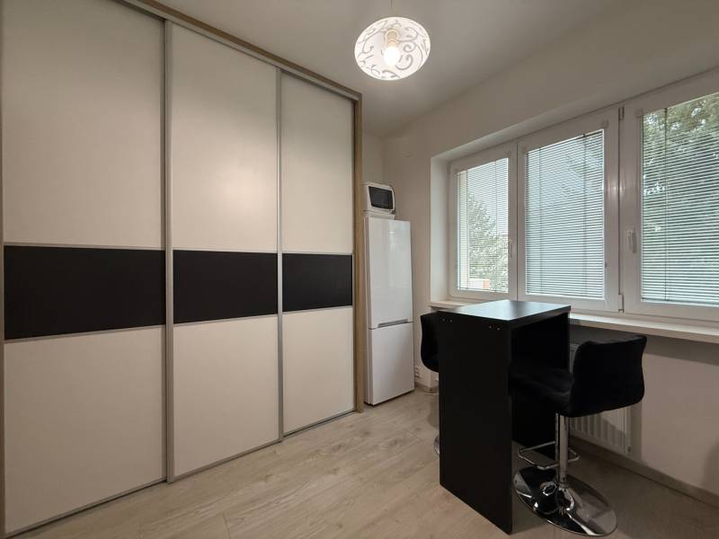 Einrichtung einer Einzimmerwohnung, Schiebetürenschrank, hoher Kühlschrank, Tisch mit zwei Stühlen.