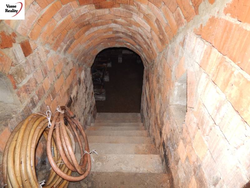 Ziegelkeller unter einem Einfamilienhaus mit Treppe nach unten und aufgerollten Schläuchen an der Wand.