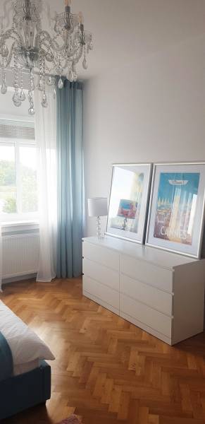 Schlafzimmer in einer Einzimmerwohnung mit Schrank, Kronleuchter und Boden in Holzoptik.