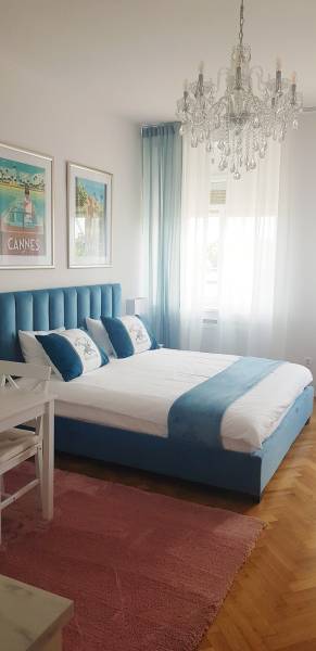 Schlafzimmer in einer Einzimmerwohnung mit blauem Bett, Kronleuchter und Holzboden.