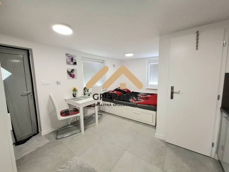 Interieur einer Hütte mit Esstisch, Stühlen und Bett auf hellem Boden.