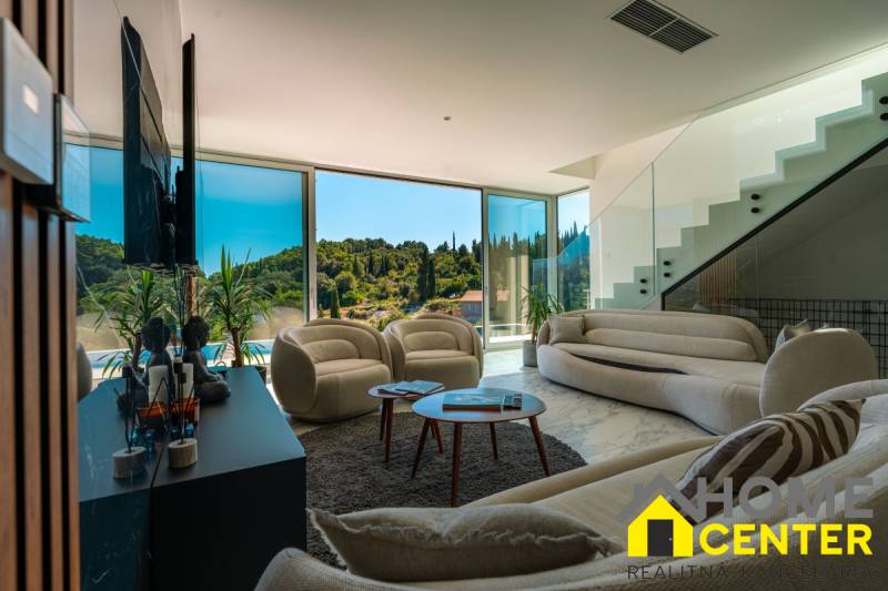 Wohnzimmer der Villa mit großen Fenstern, bequemen Sitzgelegenheiten und Blick in die Natur.