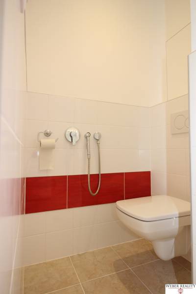 Toilette in einer Einzimmerwohnung mit beigem Boden und roten Wandfliesen.