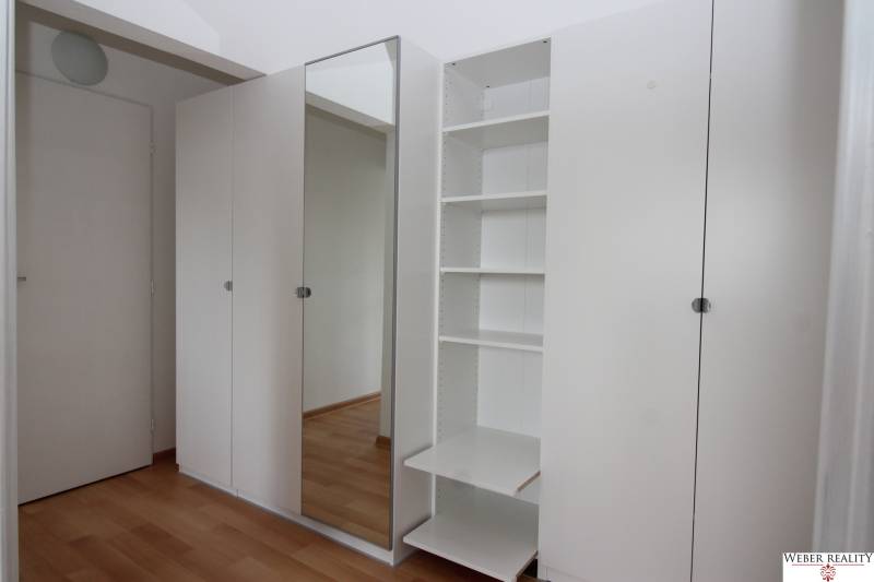 Weißer Einbauschrank mit Spiegel und Regalen in einer Einzimmerwohnung.