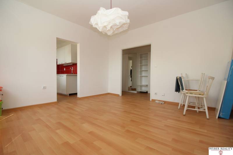 Ein Zimmer mit einem Holzboden, weißen Möbeln und einer roten Küchenwand.