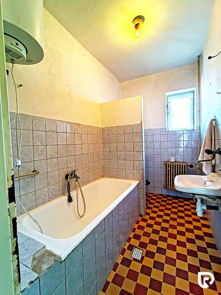 Ein Badezimmer in einem Einfamilienhaus mit einer Badewanne, einem Waschbecken, einem Heizkörper und Fliesen im Schachbrettmuster.